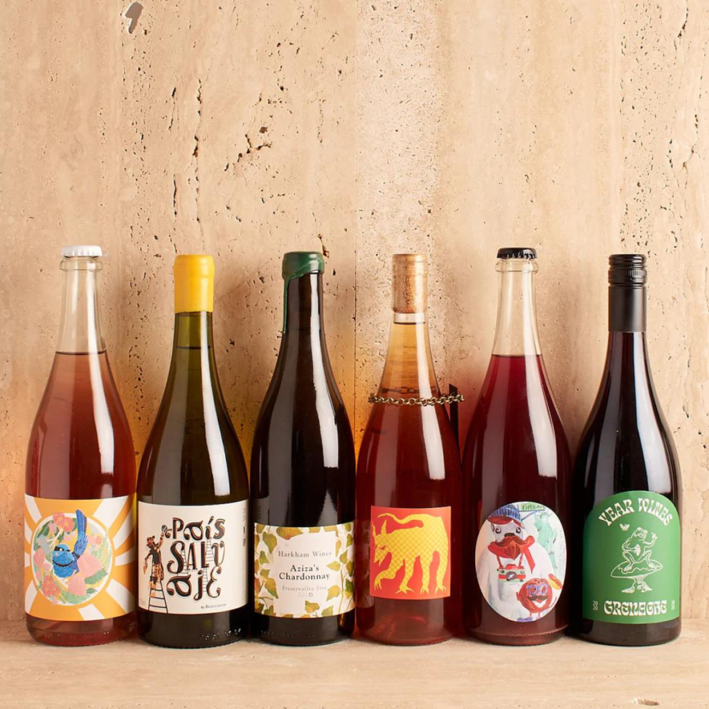 6 bottles of natural wines lined up against a neutral tan stone wall.