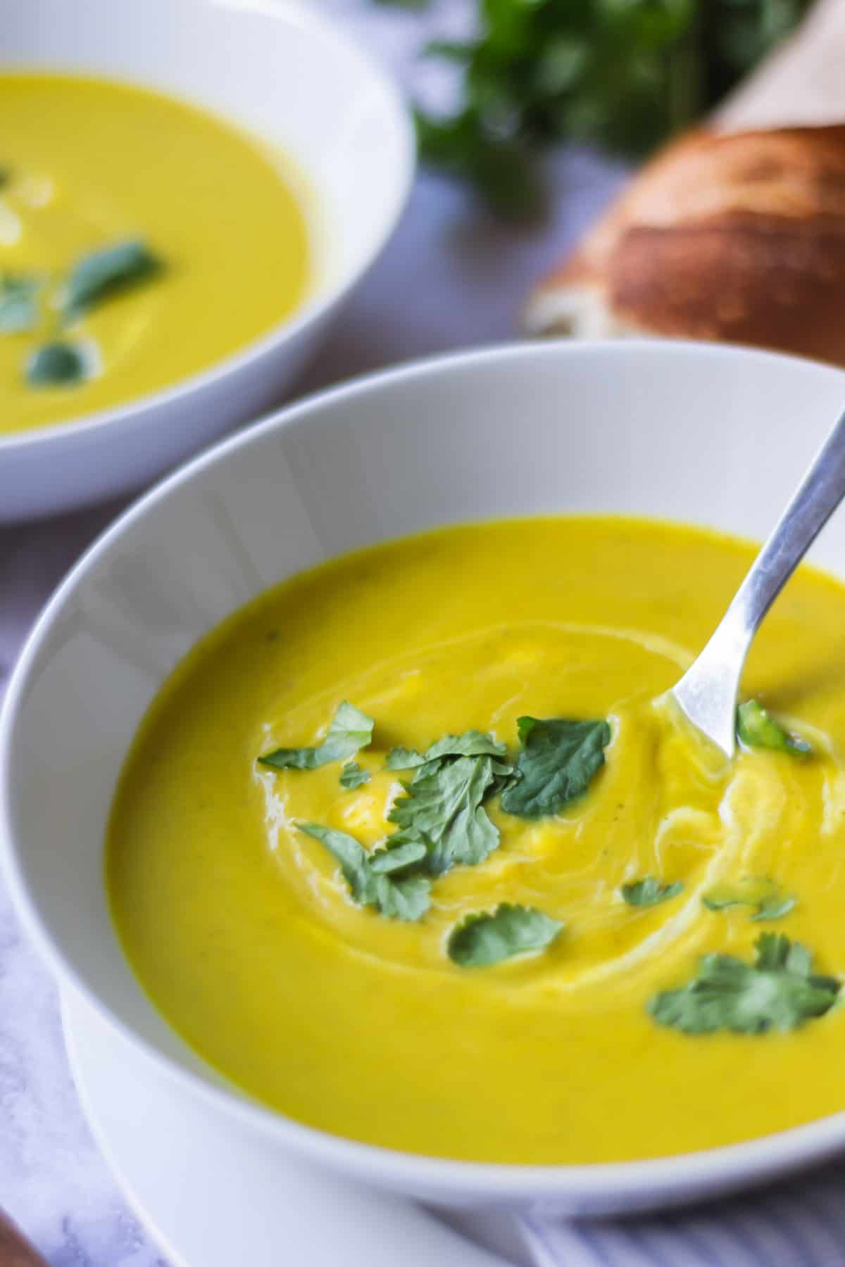 A close-up view of a white bowl filled with butternut squash and broccoli soup with coriander on top.