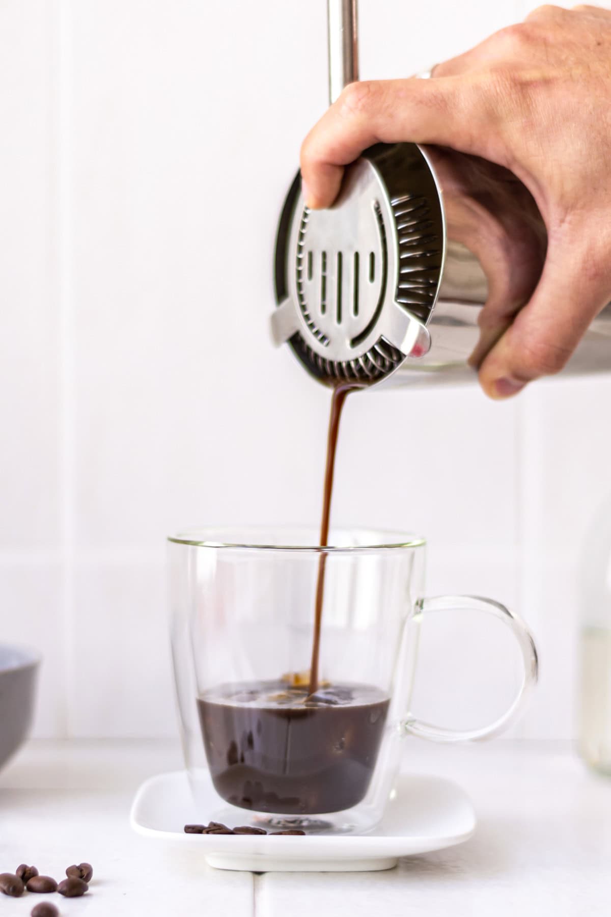 Hand pouring espresso out of a cocktail shaker, through a strainer and into a clear mug with ice.