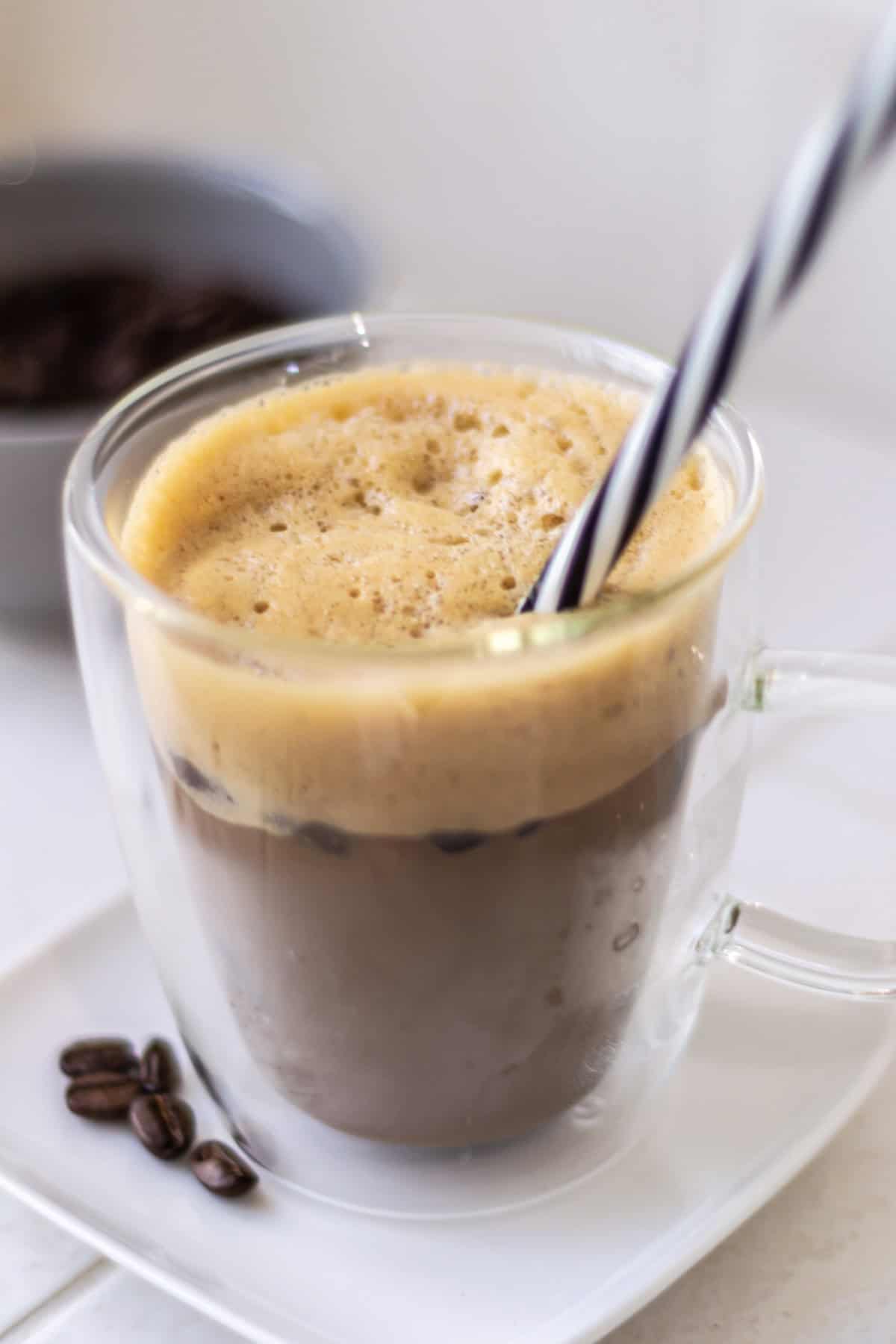 Overhead shot of iced shaken espresso with a straw in it and a lot of foam.