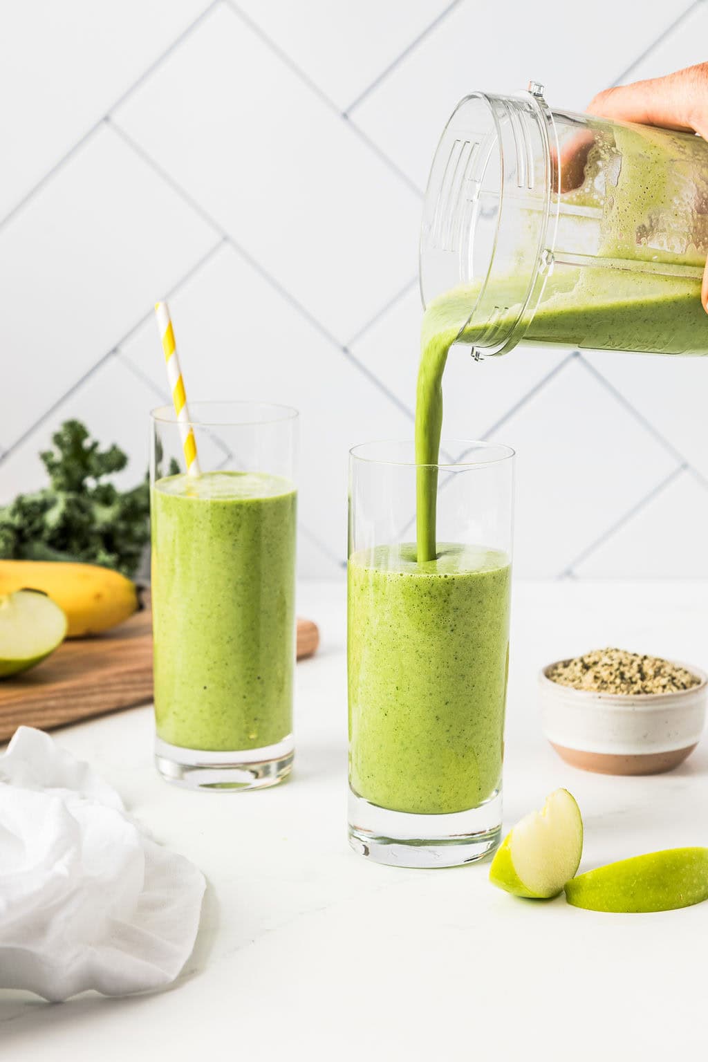 Action shot of kale apple smoothie being poured into a tall transparent glass.