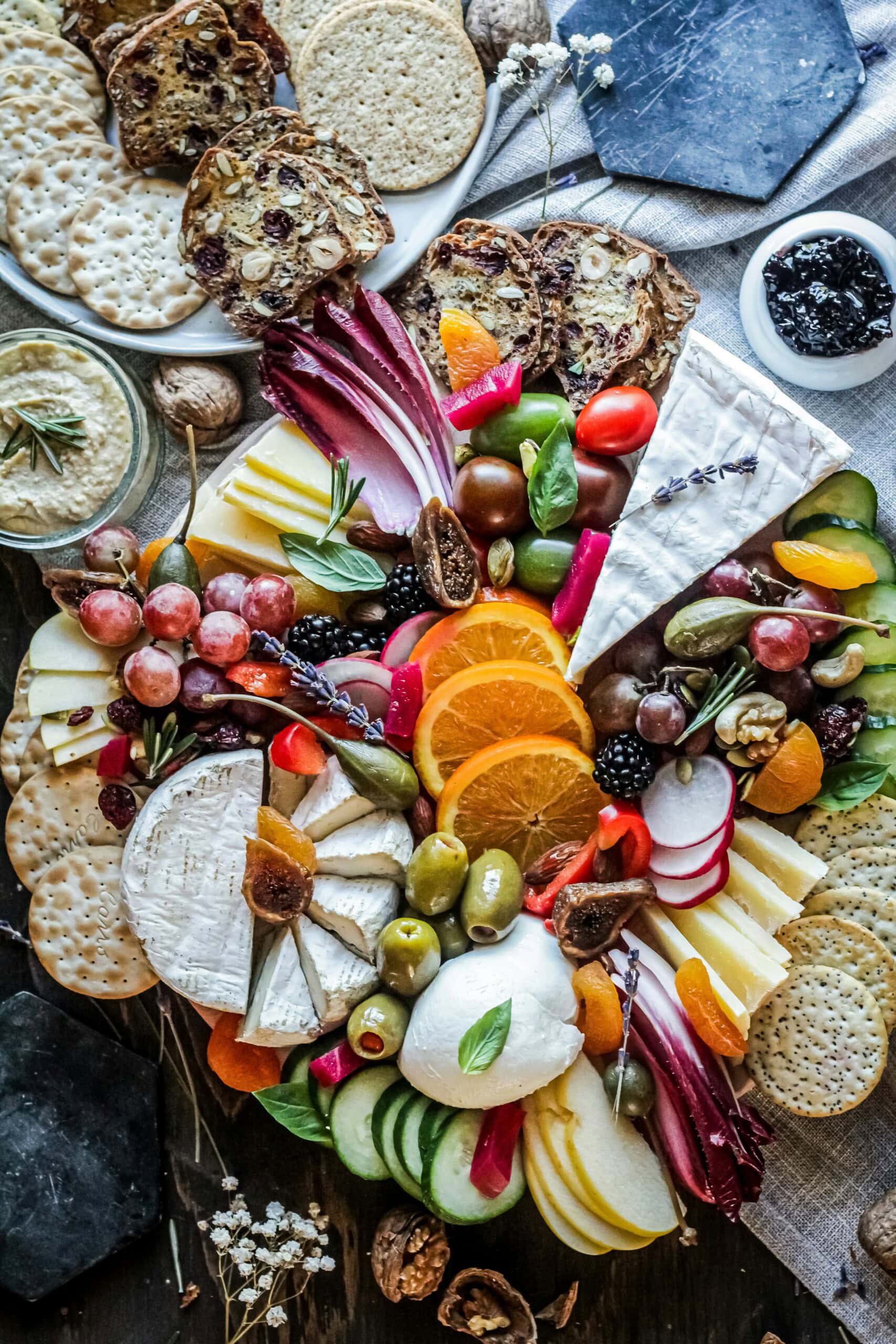 Overhead view of a delicious looking charcuterie board containing cheese, olives, grapes, crackers, vegetables and fruit.