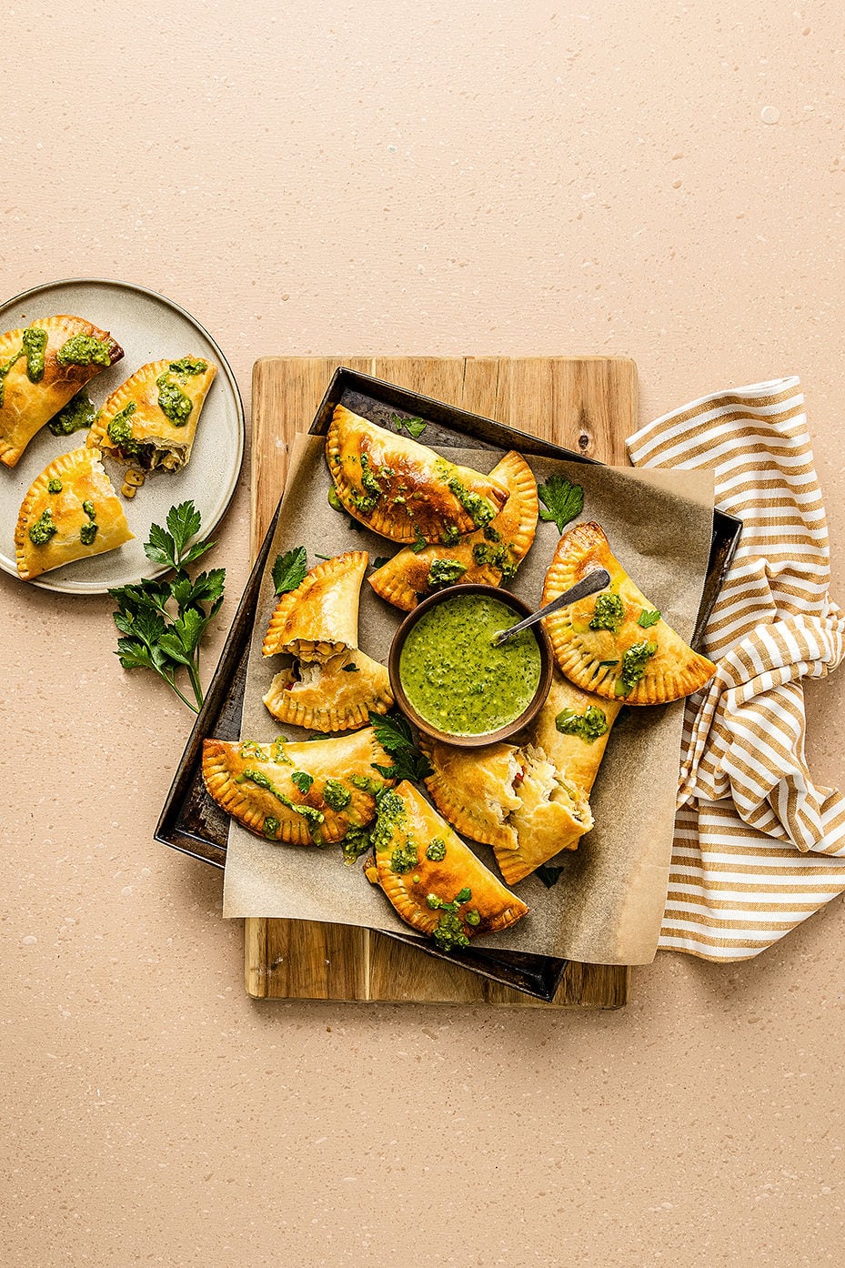 Overhead view of vegetarian empanadas on a baking tray with chimichurri sauce.