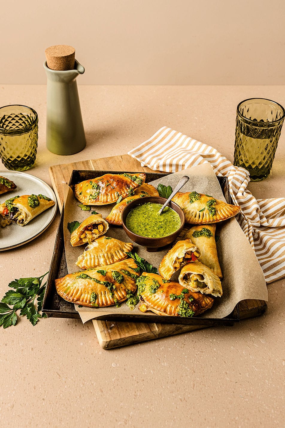 Angled view of vegetarian empanadas on a baking tray, with chimichurri sauce.