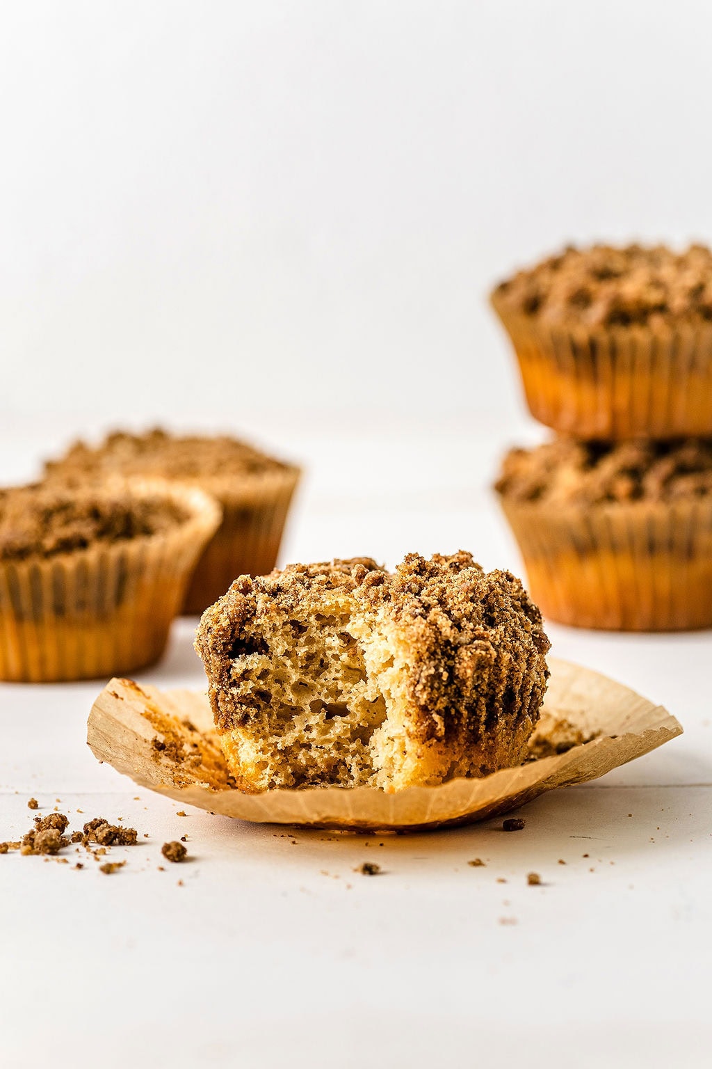Front view of a coffee cake muffin with crumb topping, with a bite taken out of it and other muffins in the background.