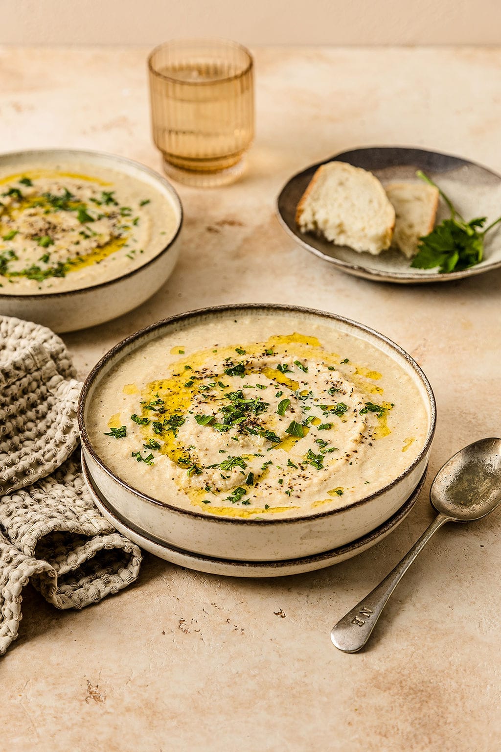Front view of creamy cauliflower soup with a drizzle of olive oil on top, a plate of bread is in the background.