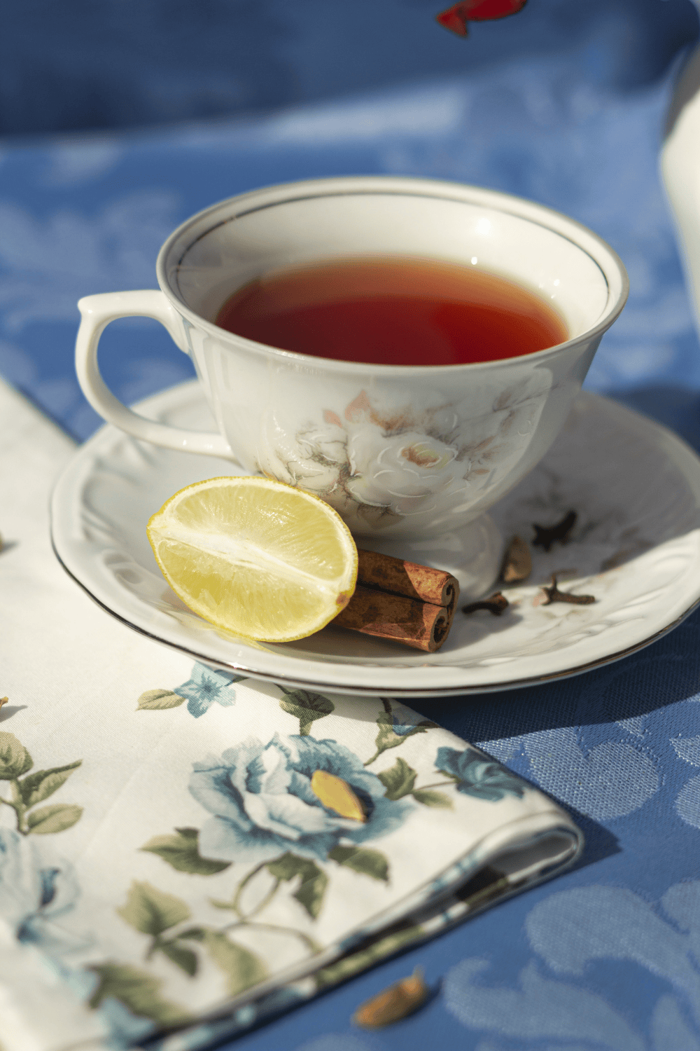 Front view of a cup of tea in a china cup, with a lemon and cinnamon stick on a platter.