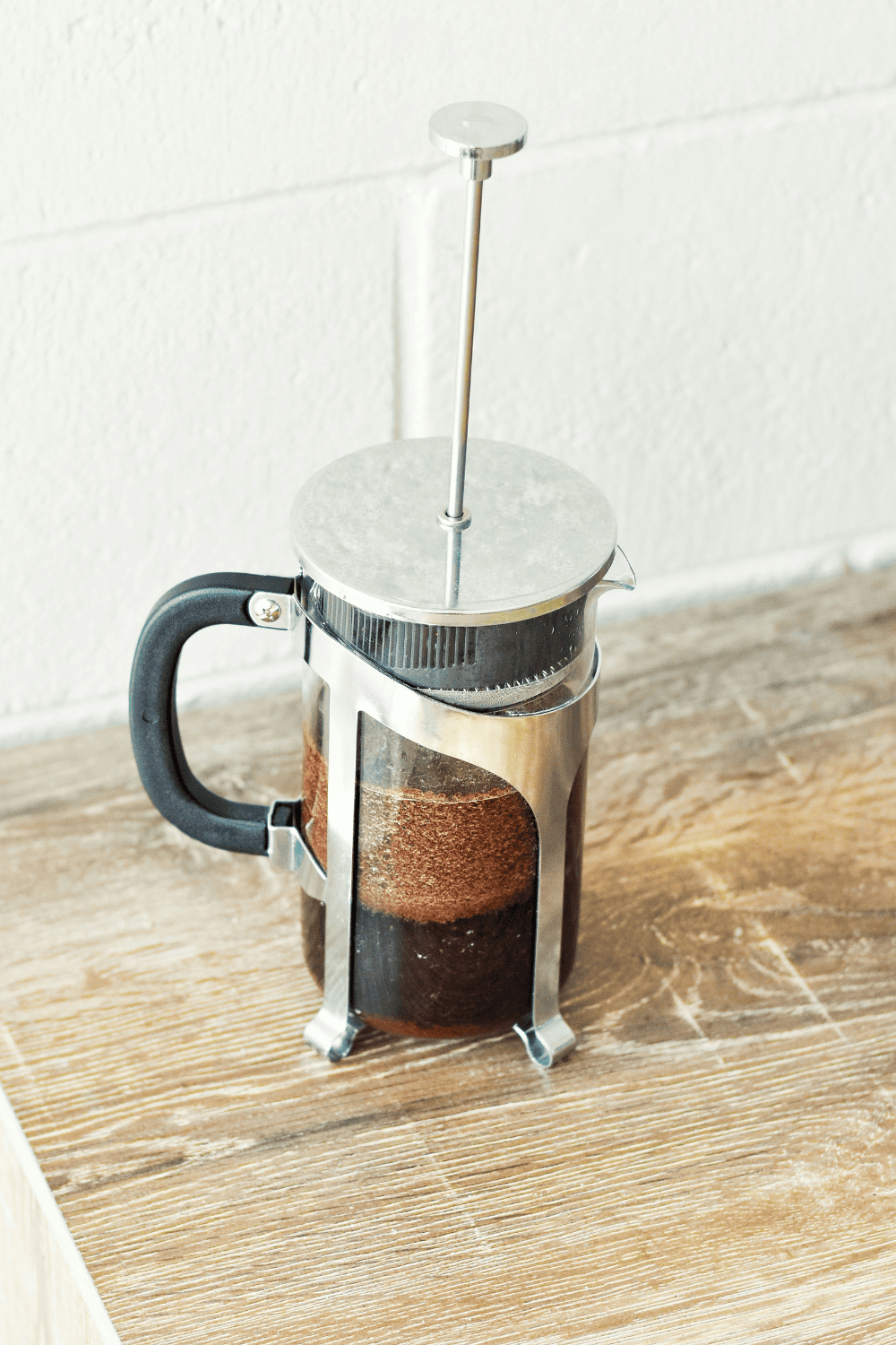 Photo showing a French Press sitting on a wooden table, brewing coffee.