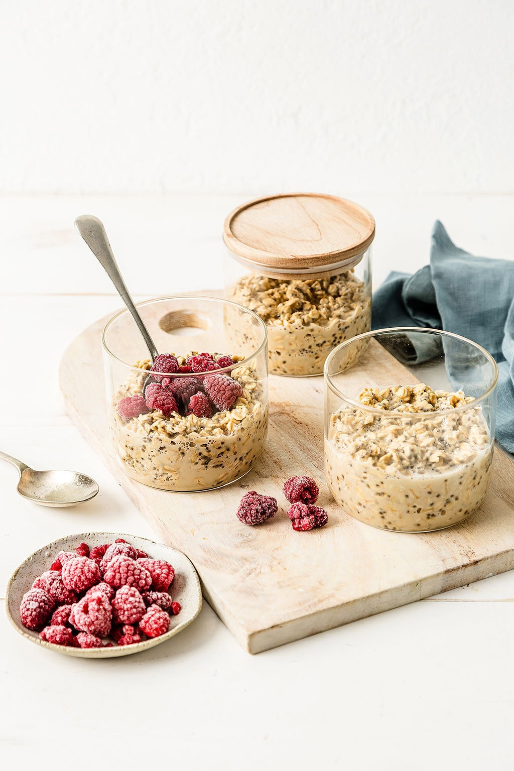 Three jars of meal prep overnight oats, one with raspberries on top and a bowl of raspberries in the foreground.