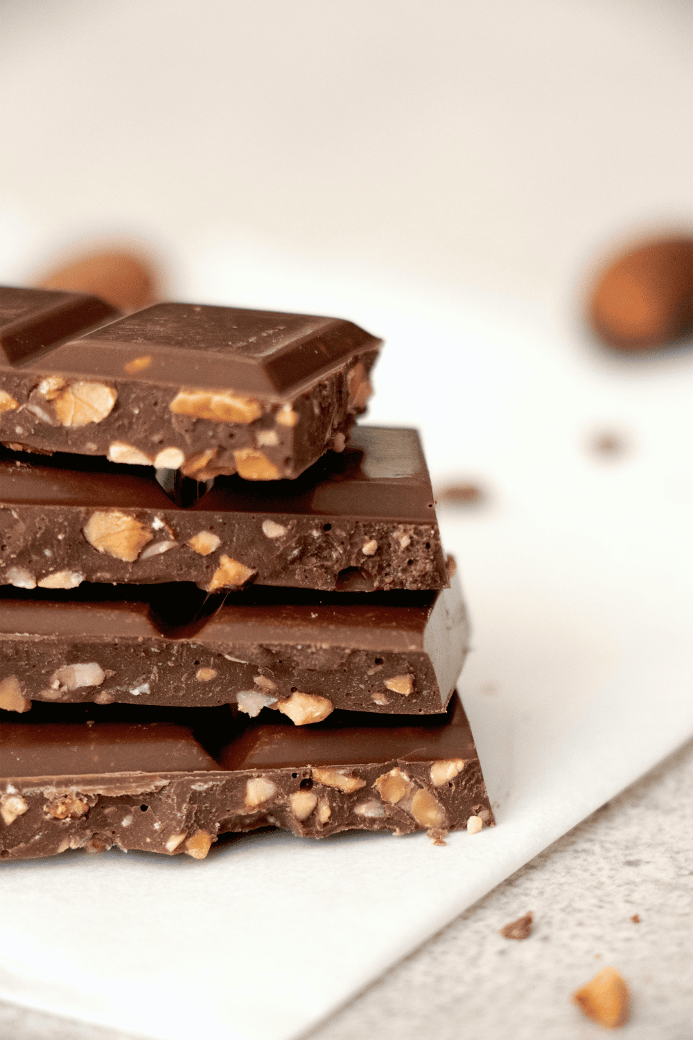 Close up of chocolate bar squares stacked in a pile. You can see nuts inside, and a delicious-looking cross-section of the bar.