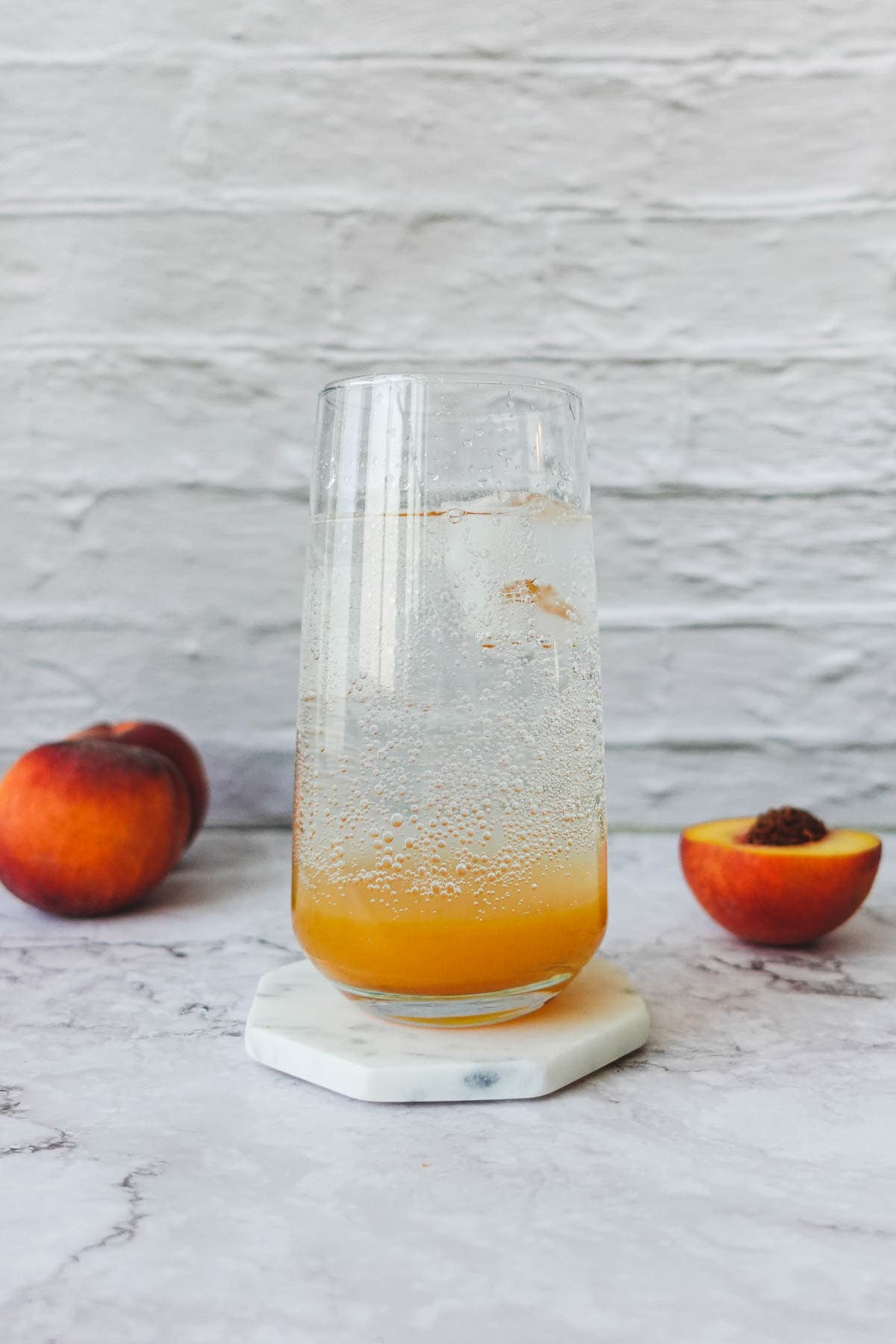 Front view of a peach soda with peach syrup in the bottom of the glass and soda water in a highball glass.
