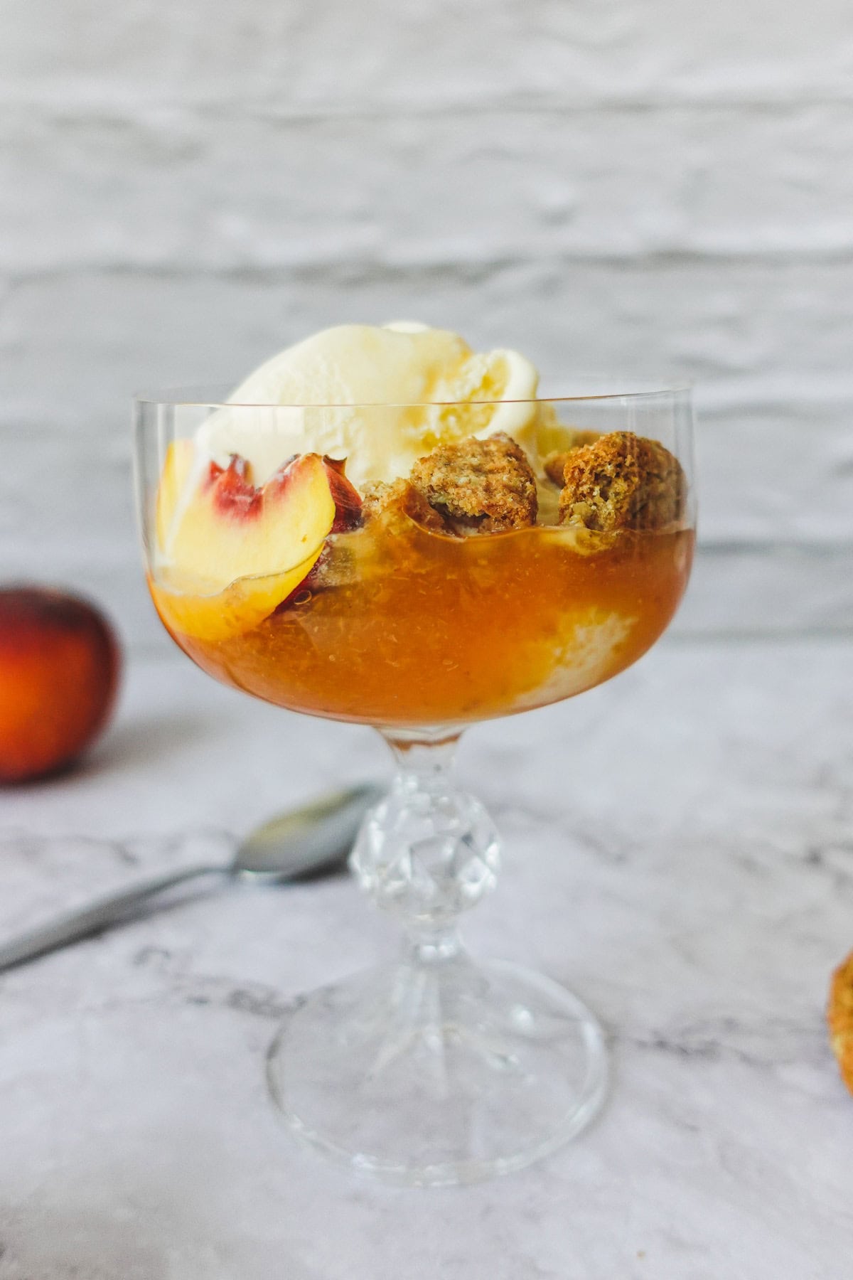 Front-view of a Peach sundae in a glass with peach slices, vanilla ice cream and oat cookies.