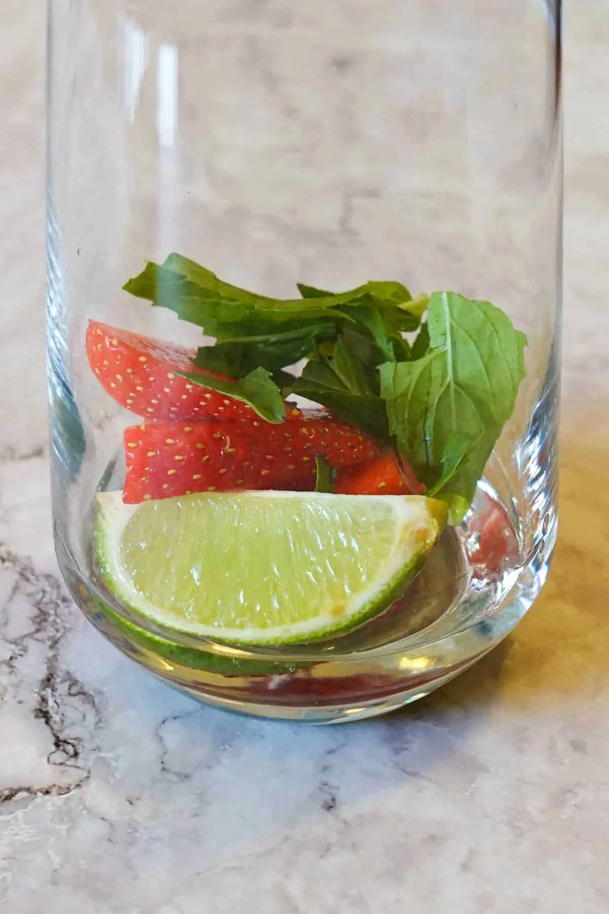 Closeup of lime wedge, strawberry slices and mint leaf in a glass.