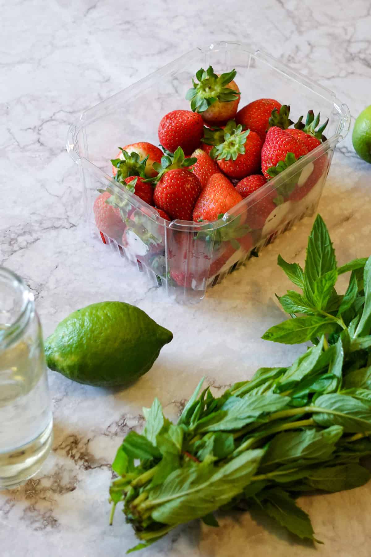 Photo of ingredients for a virgin strawberry mojito, including mint, lime, strawberries and simple syrup.