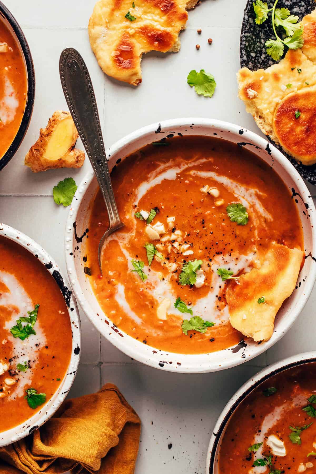 Overhead shot of spicy pumpkin tomato soup in a bowl on a white table with flatbread dipping into it.