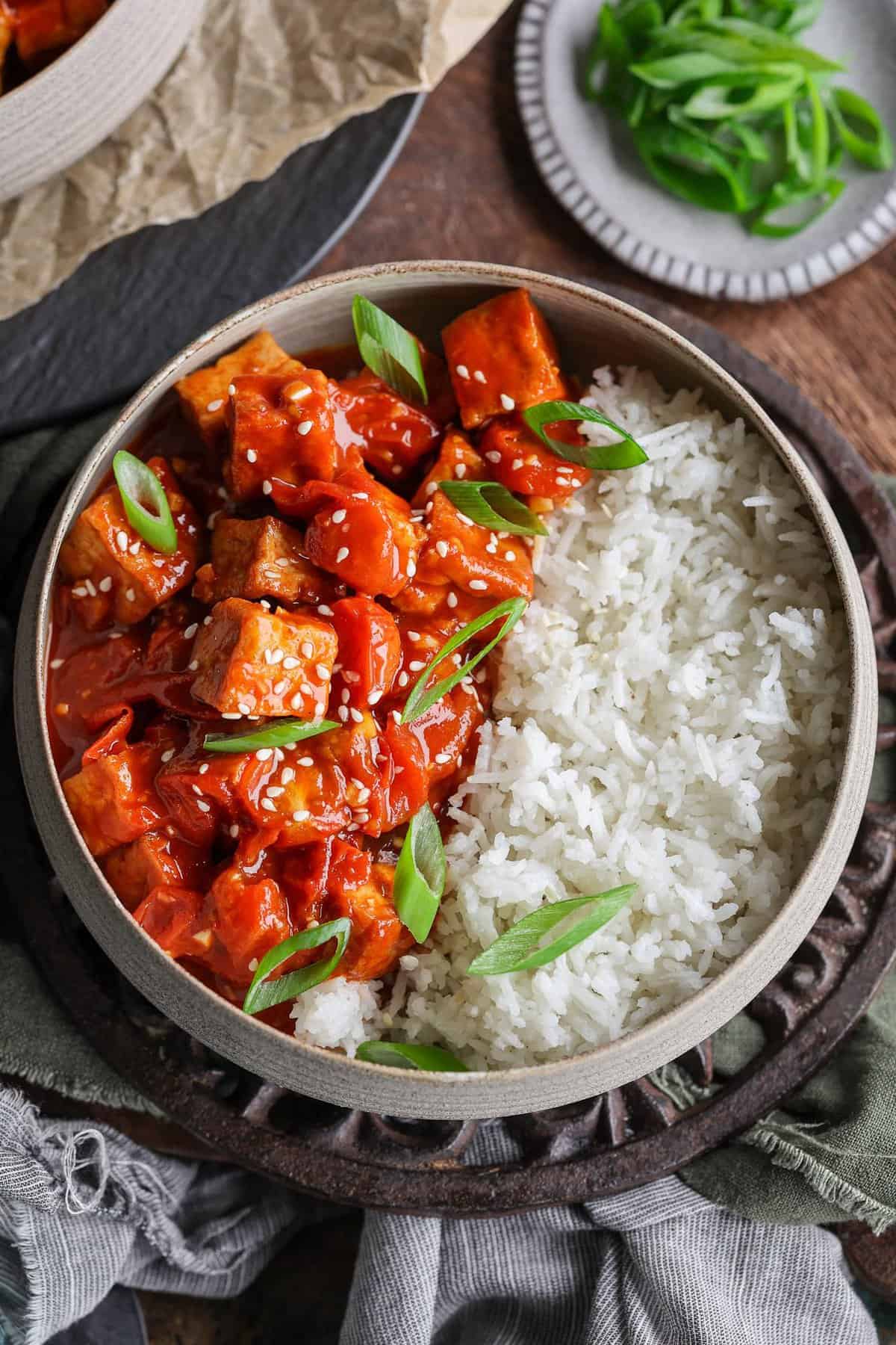 Overhead shot of bowl, filled half with rice, half with spicy tofu and green onions sprinkled on top.