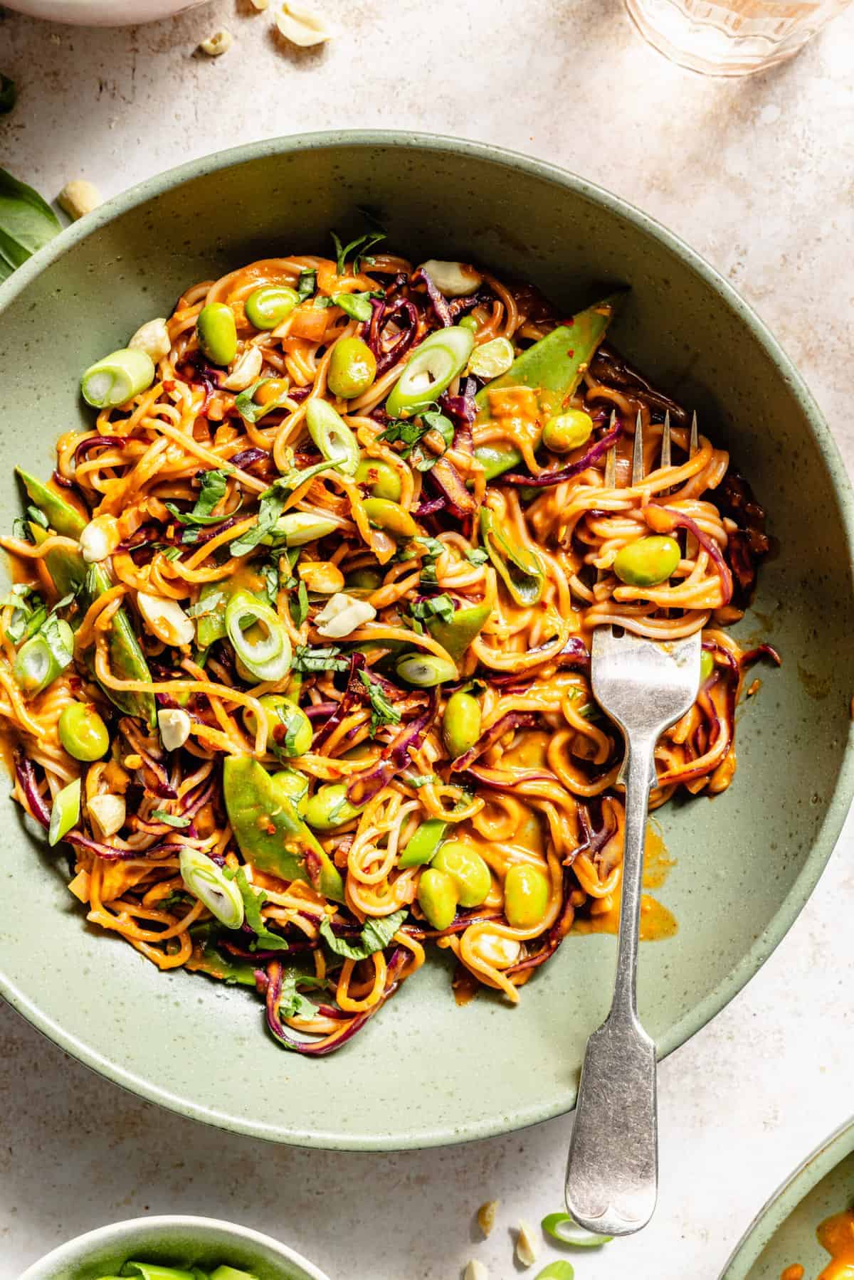 Overhead shot of peanut noodles in a green bowl with edamame, cabbage and snap peas.