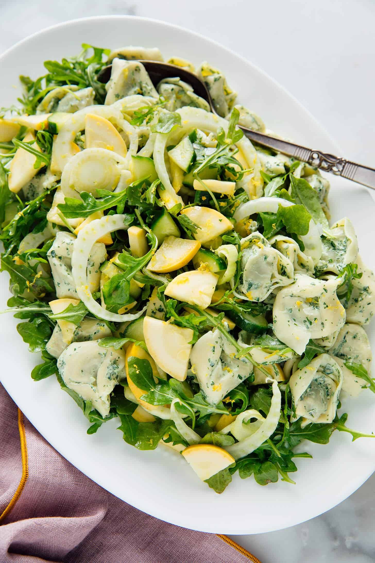 Overhead shot of tortellini salad on a white oval plate with a silver serving spoon.
