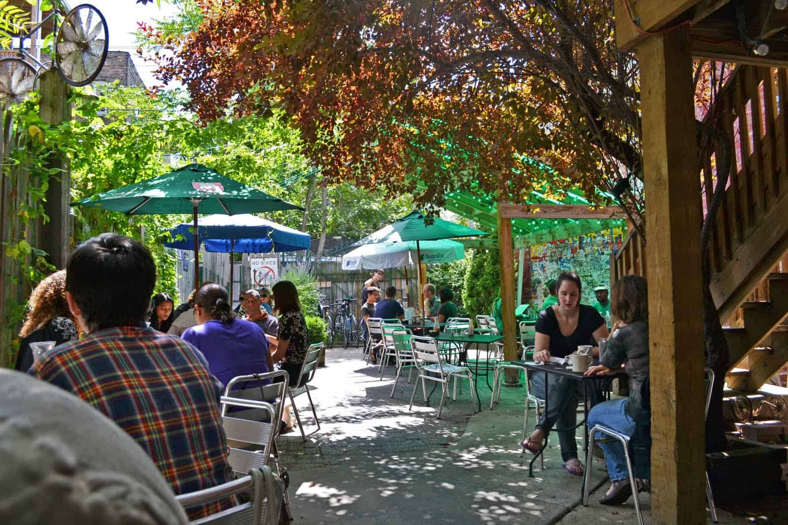 View of the outdoor area of Handlebar, with several tables with green, white and blue umbrellas and lots of people enjoying their meals.