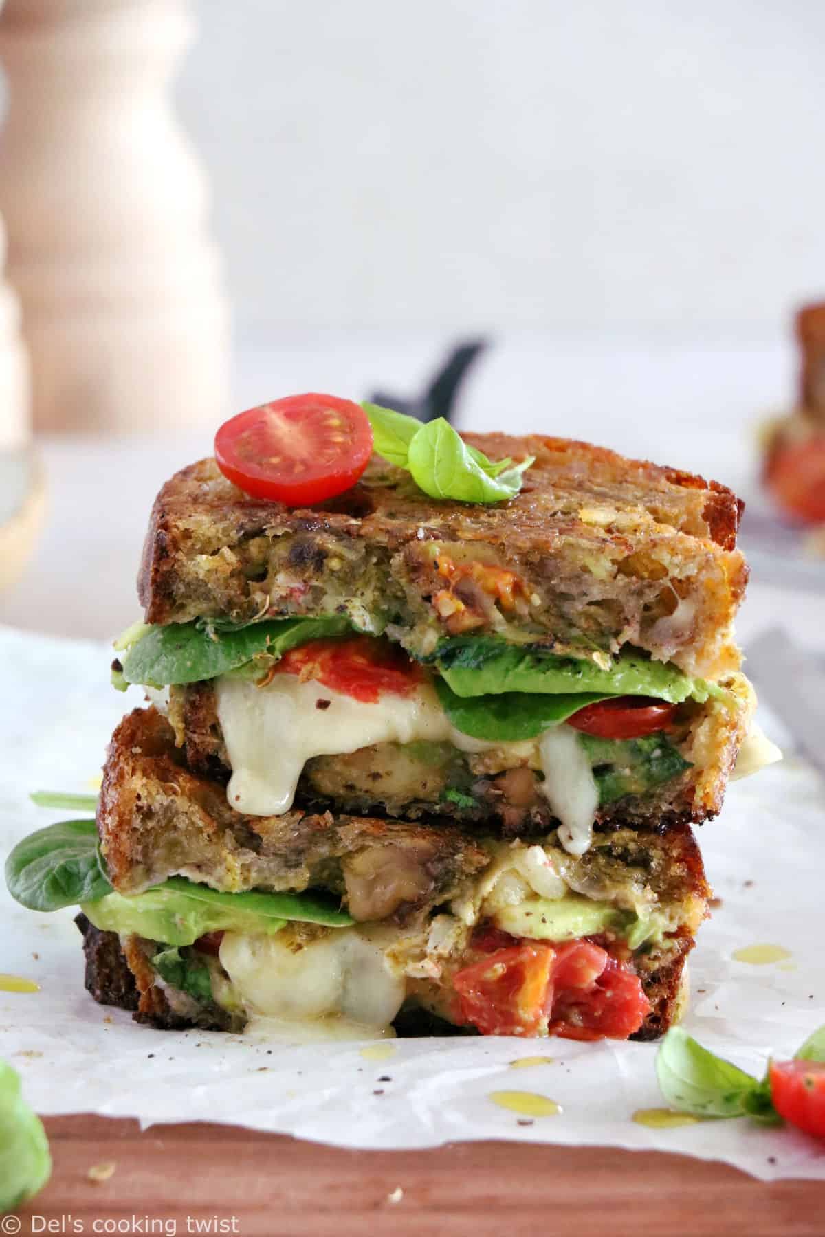 Front view of the cross section of a grilled cheese with spinach, cheese, tomato and pesto oozing out.