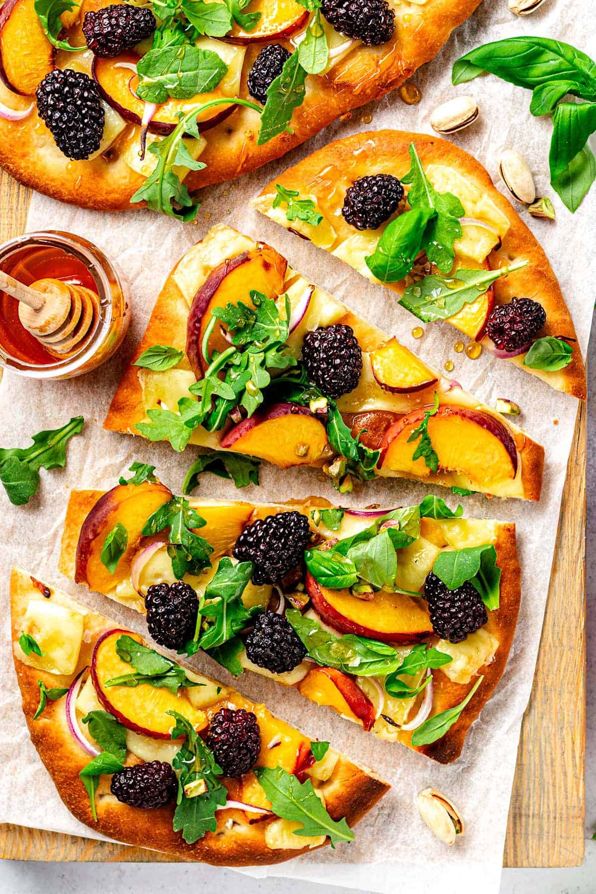 Overhead shot of a flatbread with arugula, peach, blackberries and a jar of honey on the side.
