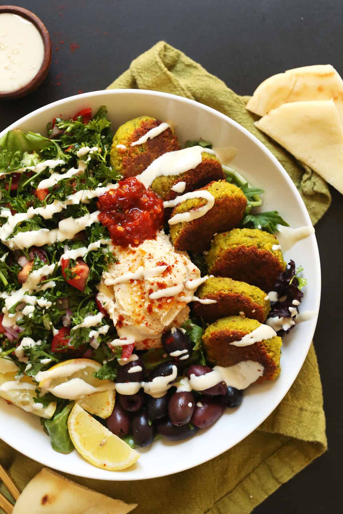 Overhead shot of a Mediterranean bowl from Minimalist Baker with falafels, hummus, olives and greens.
