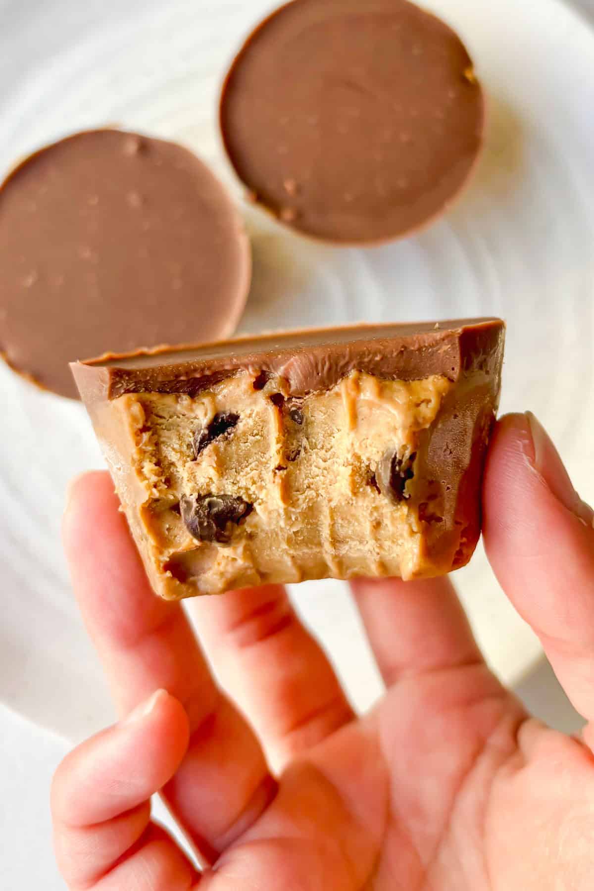 Front view of a cookie dough cup with a chocolate topping and a bite taken out of it.