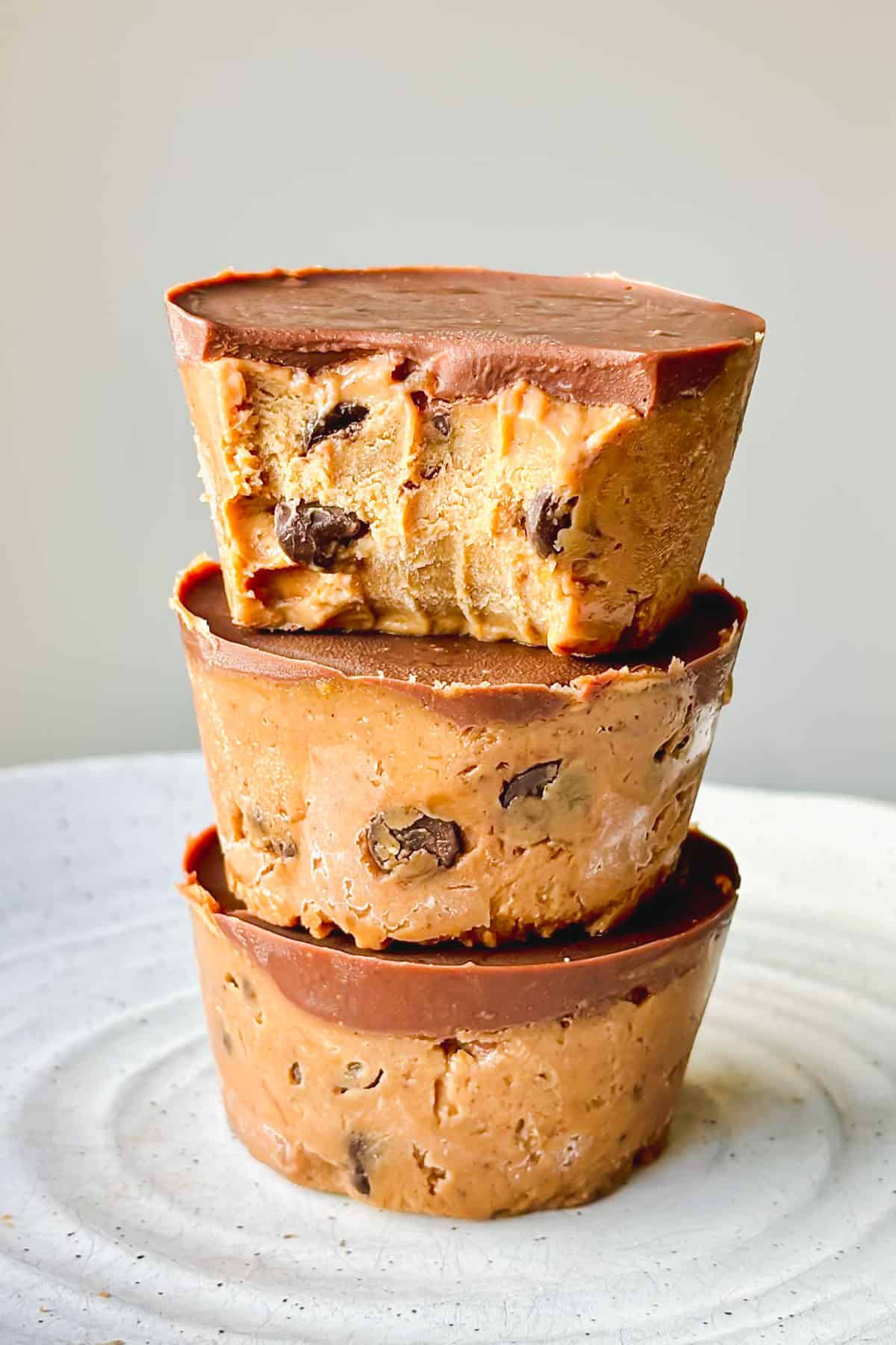 Three cookie dough cups piled on top of each other on a white plate.