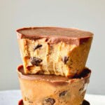 A cookie dough cup sitting on top of another cookie dough cup against a light grey background.