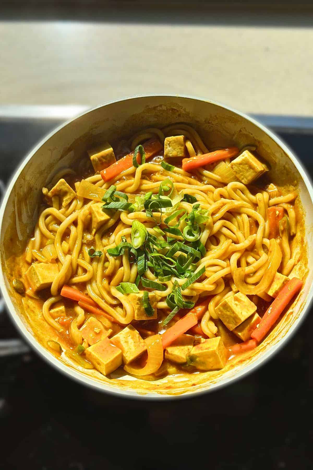 Overhead shot of stir-fried curry udon in a pan with tofu, carrots, and scallion.