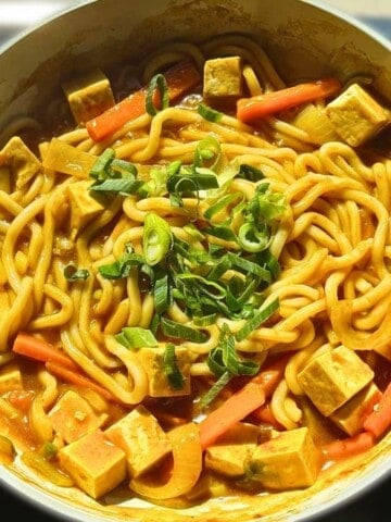 Overhead shot of stir-fried curry udon in a pan with tofu, carrots, and scallion.