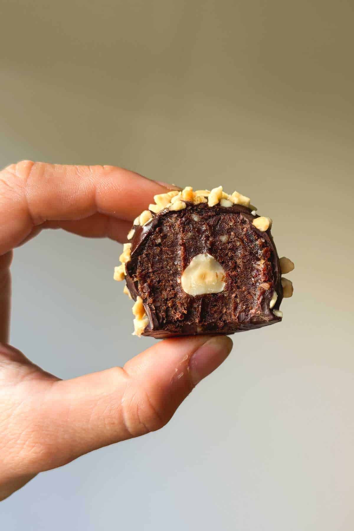 Cross-section view of a Ferrero Rocher protein ball with a bite taken out of it, showing a hazelnut in the centre.