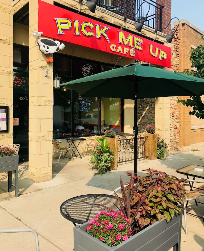 Outside view of Pick Me Up Cafe in Chicago with a green umbrella and flower planters outside.