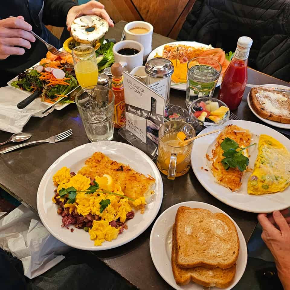 Overhead shot of food on the table at Tweet in Chicago including hash, toast, omelet, salad, bagel fruit salad, mimosas and coffee.