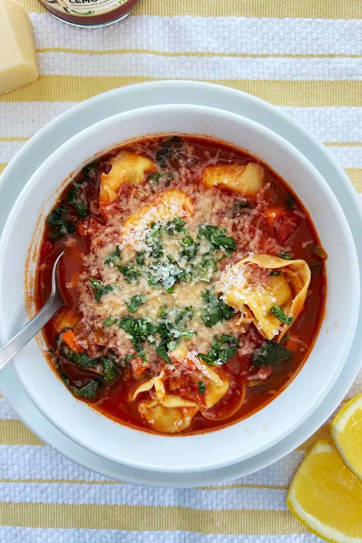 Overhead shot of vegetarian tortellini soup topped with parmesan and coriander in a white bowl.