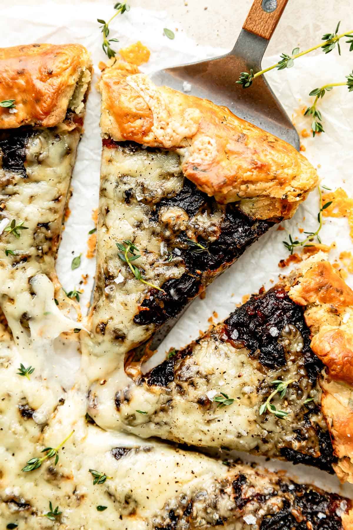 Overhead shot of a French onion galette on a white background, with a slice being cut out of it.