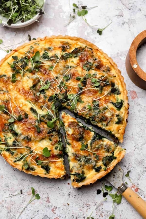 Overhead shot of a quiche florentine, with a slice cut out of it, on a marble table.
