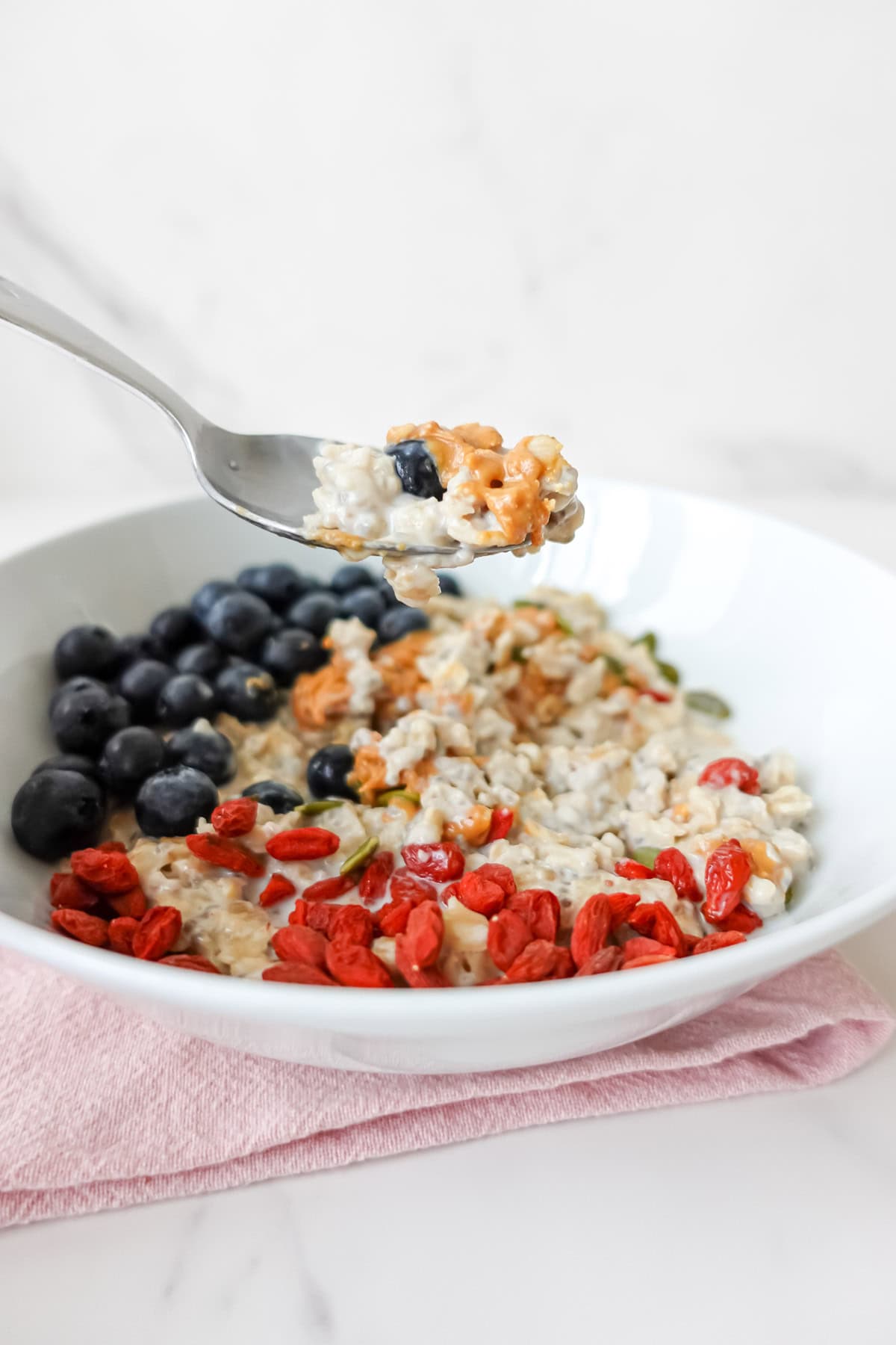 Front view of a bite of almond milk porridge on a spoon with a blueberry and peanut butter.