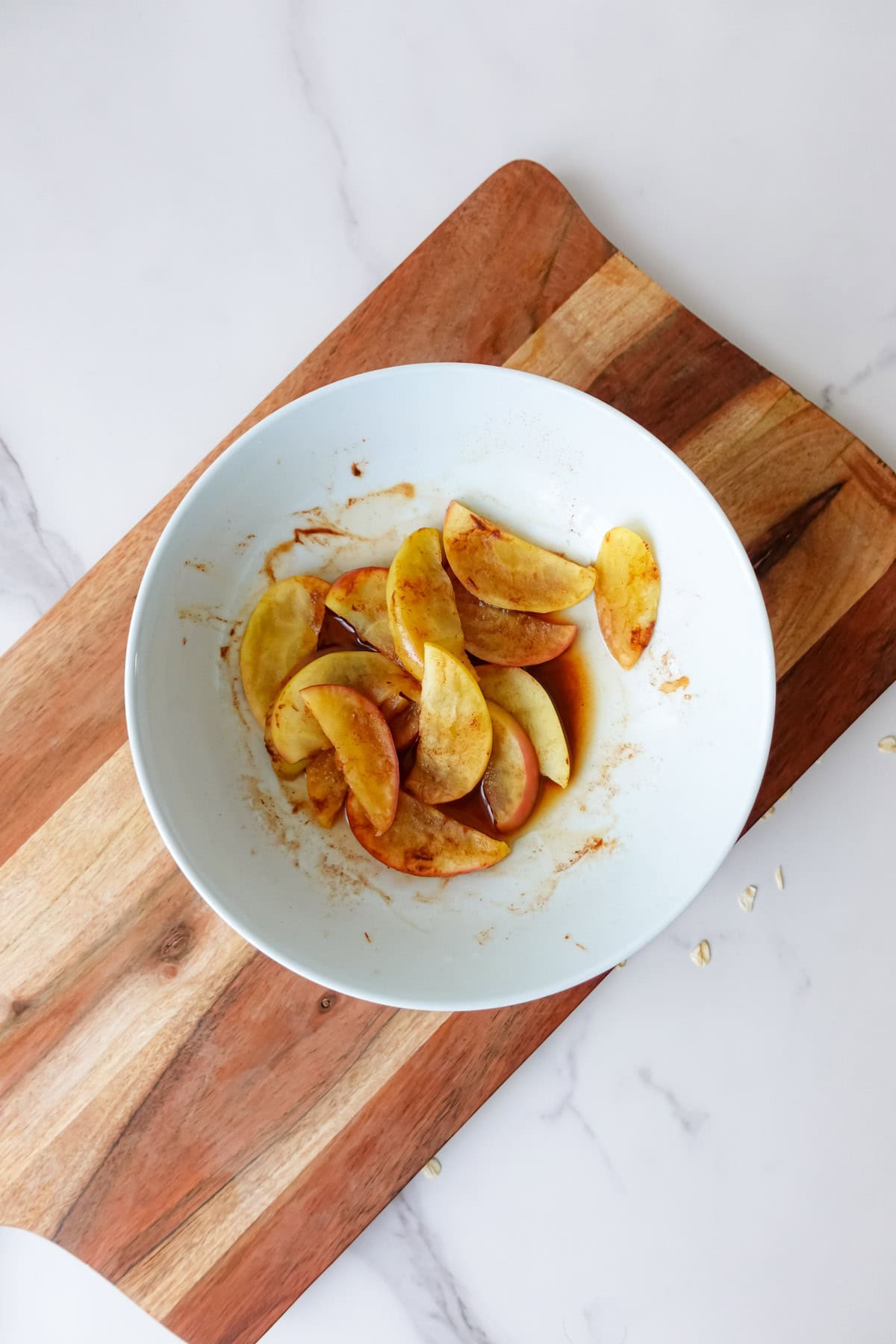 Overhead shot of cooked cinnamon apples in a white bowl on a wooden cutting board.