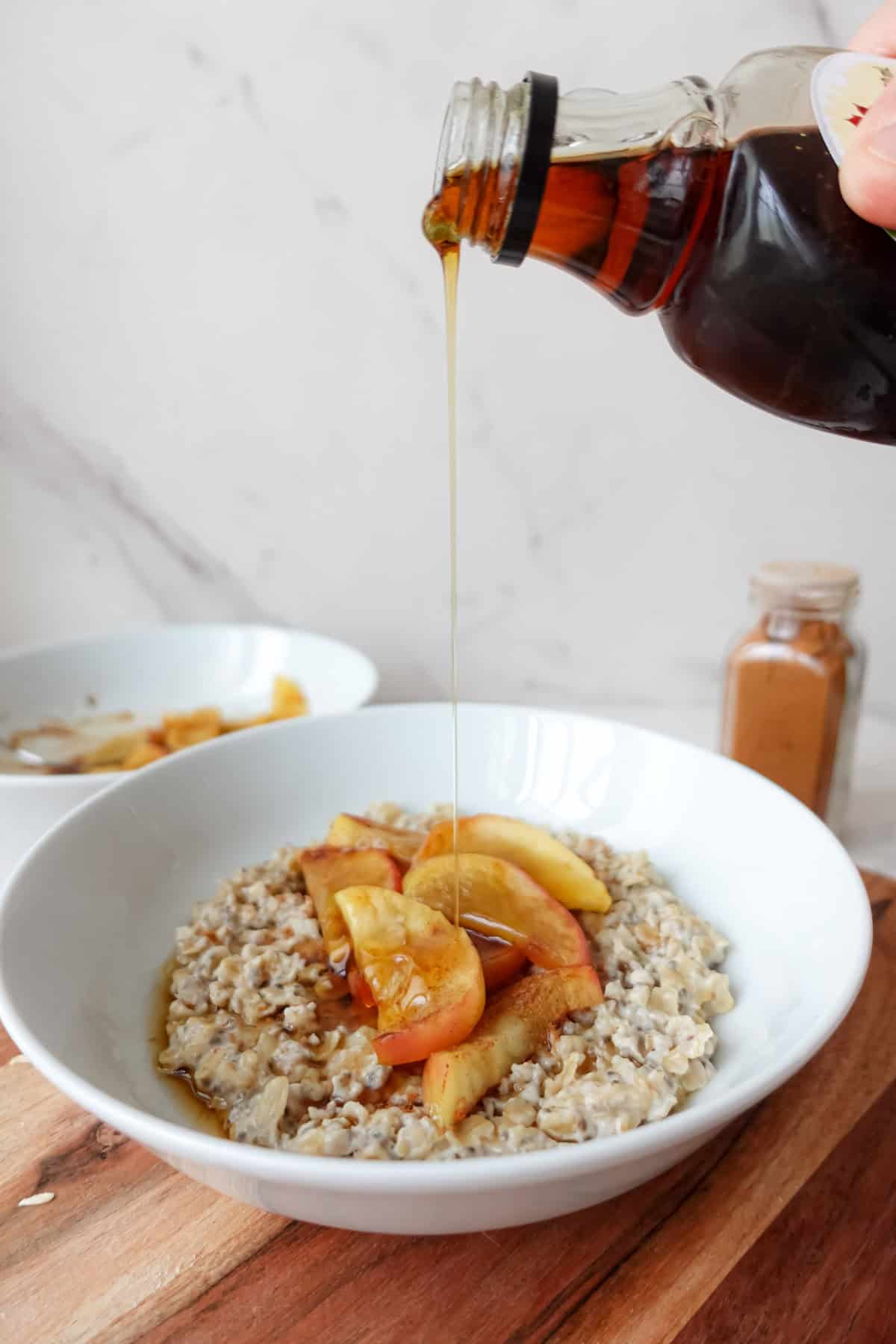 Front view of maple syrup being poured over a bowl of apple porridge.