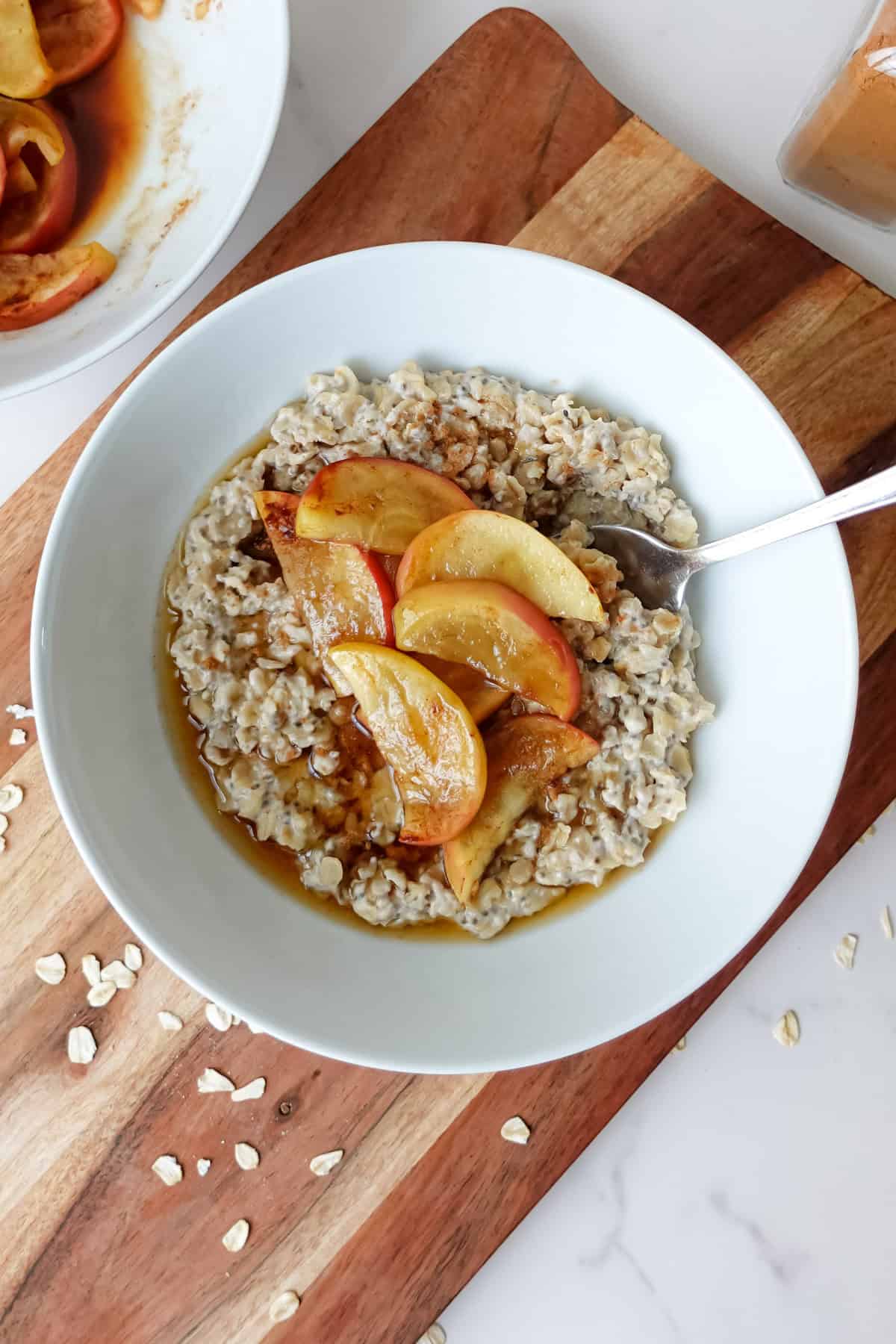 Overhead view of apple porridge in a white bowl, sitting on a wooden cutting board.
