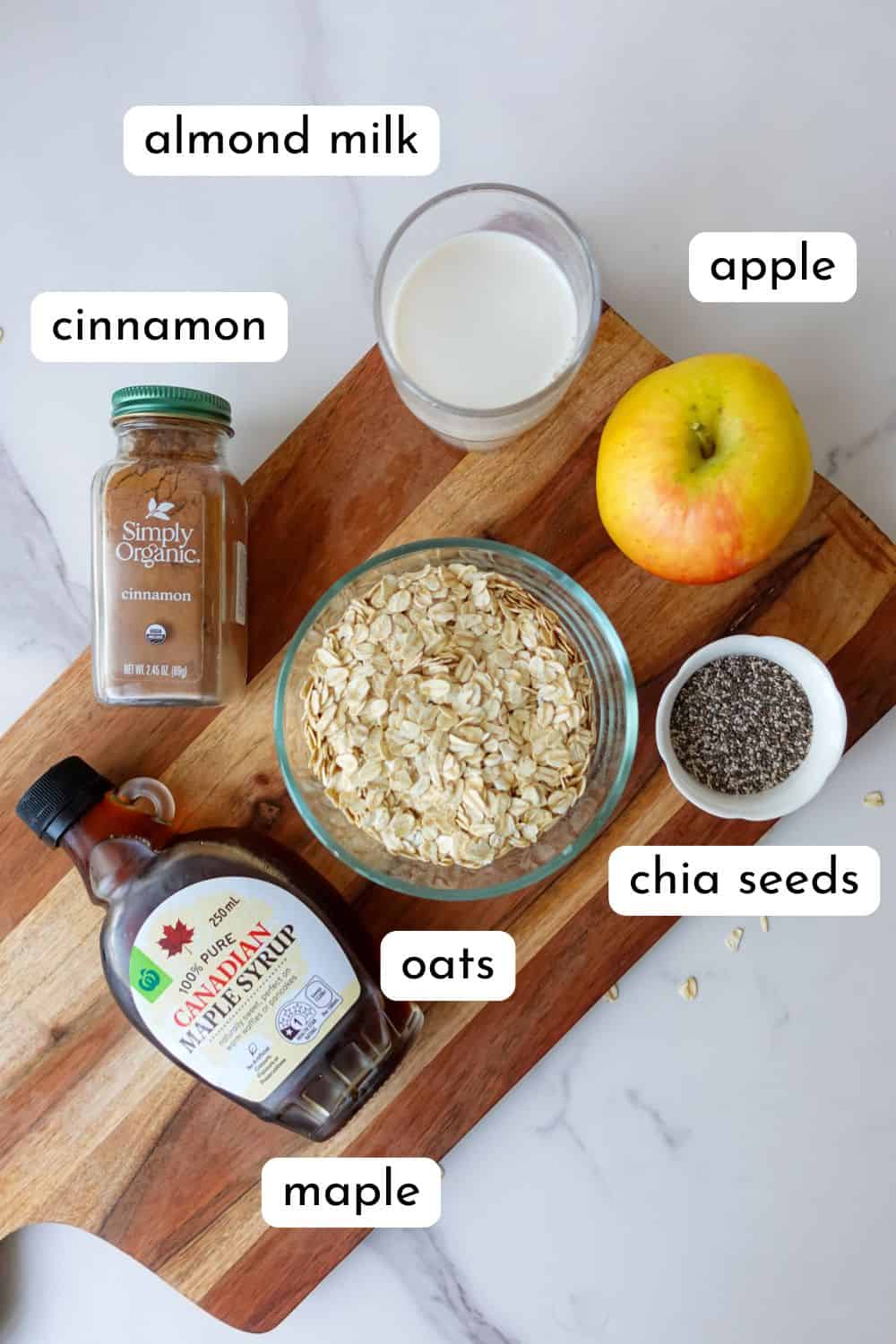 Flatlay of apple porridge ingredients, labelled, including: cinnamon, almond milk, apple, chia seeds, oats, maple and cinnamon.