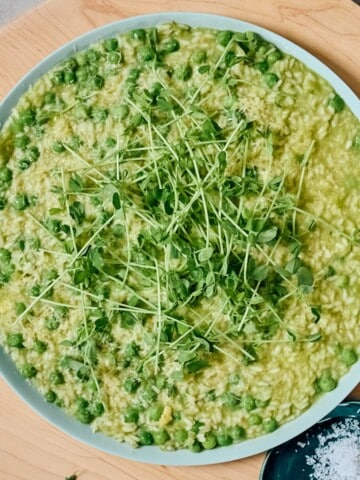 Overhead shot of pea and leek risotto in a bowl, topped with pea tendrils.