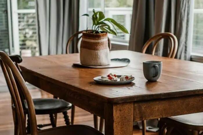 Inviting dining room featuring a wooden table, chairs, and a coffee mug, with natural light from large windows.