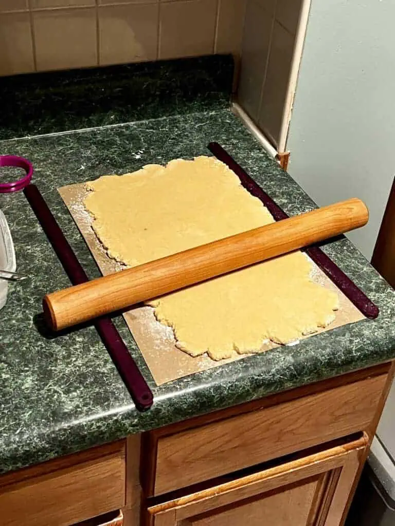 Cookie rollout setup with raw dough rolled out on parchment paper with rolling guides and a rolling pin
