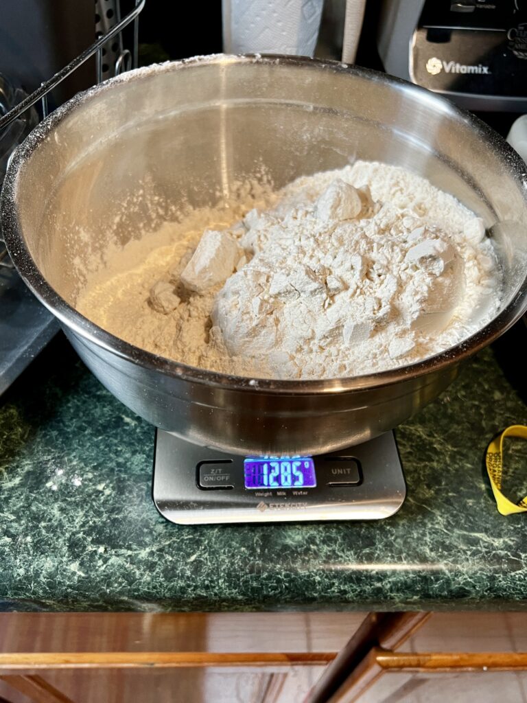 Flour in a large mixing bowl weighed on top of a kitchen scale