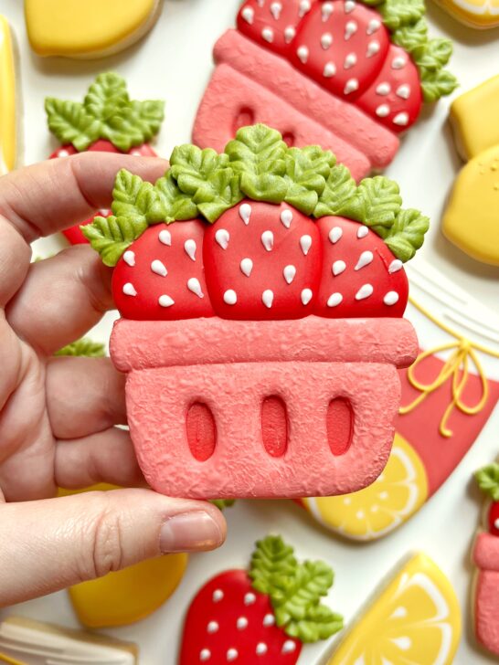 Royal icing cookie depicting a basket of strawberries with red, pink, green and white icing