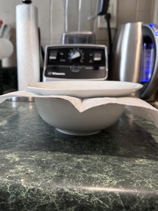 picture of a salad bowl topped with a paper towel topped with a plate to seal it to store royal icing