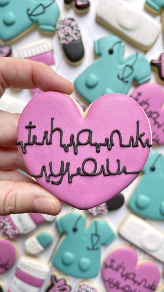 heart cookie decorated with royal icing lettering that says thank you 