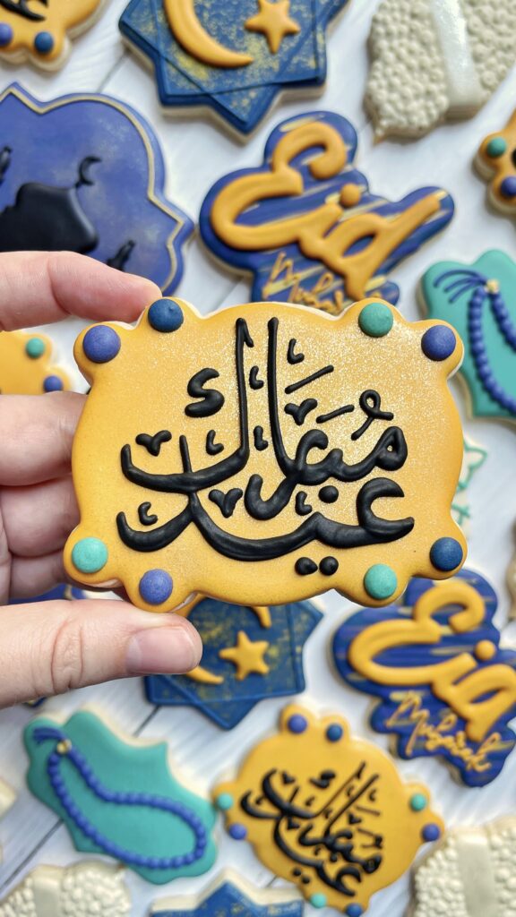 cookie decorated with royal icing lettering in arabic that says Eid Mubarak